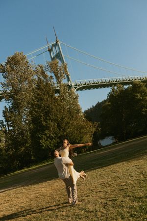 A figure performs a graceful dance pose on a grassy hillside against a bright blue sky and trees at dusk.