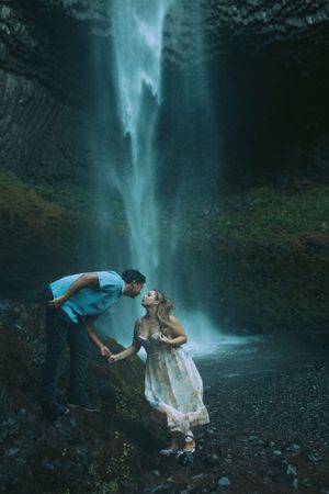 A mystical dance performance unfolds beneath a cascading waterfall in a moody forest setting.