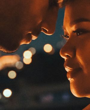Two people face each other intimately at night with bokeh city lights glowing softly in the background.