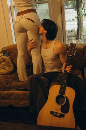 A person sits on a brown couch while holding an acoustic guitar in warm lighting with multiple frame composition.