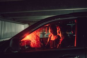 Red glow from car interior lights illuminates the passenger side window of a vehicle at night.