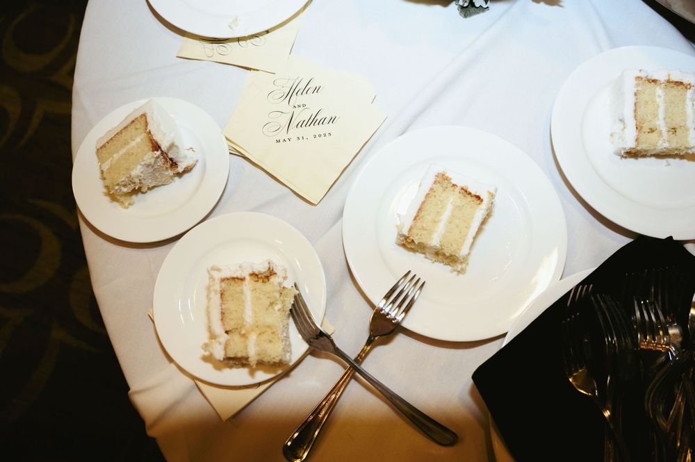 Several plates with slices of layered white cake set on a table with a fork and what appears to be table cards.