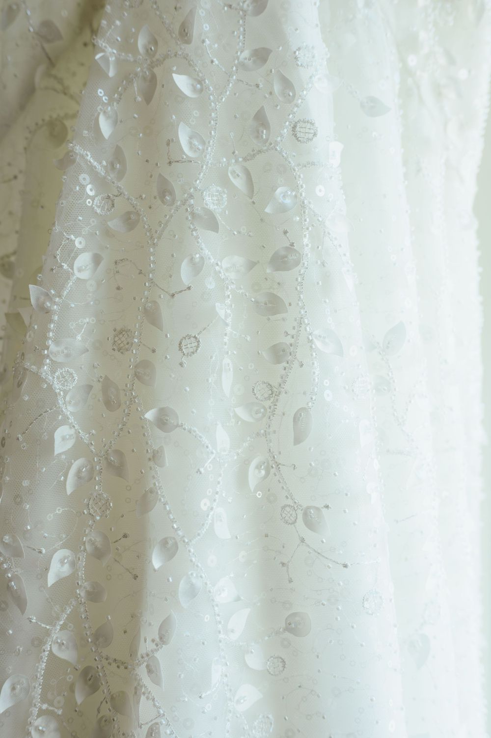 Close-up detail of white lace fabric with delicate floral embroidery patterns and sheer texture.