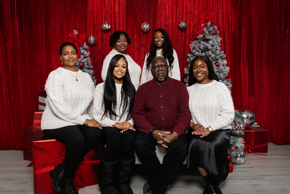 Family holiday portrait session with red curtain backdrop and silver Christmas decorations.