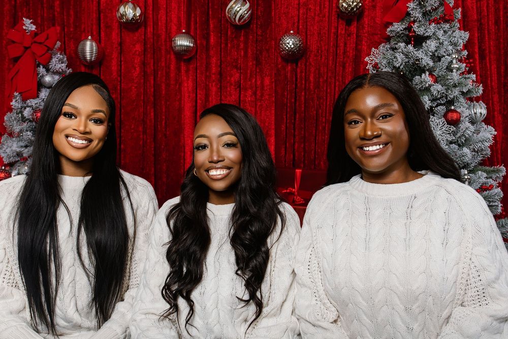 Group wearing matching white sweaters poses for holiday photos with festive red backdrop.