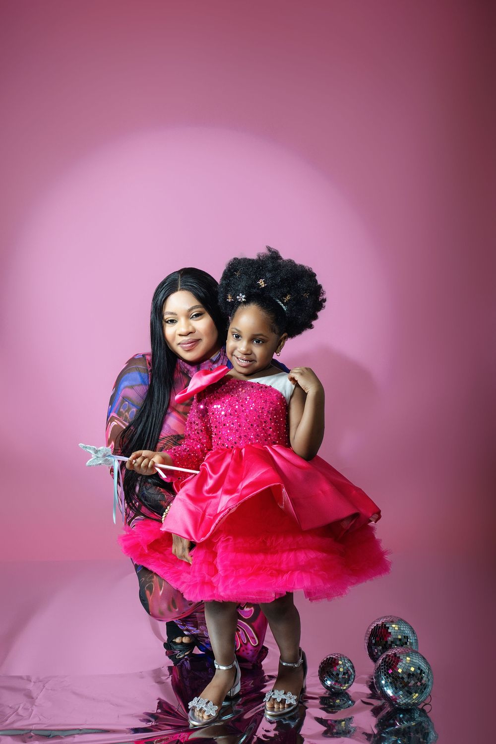 Mother and daughter in matching outfits posing with silver ornaments against pink background.
