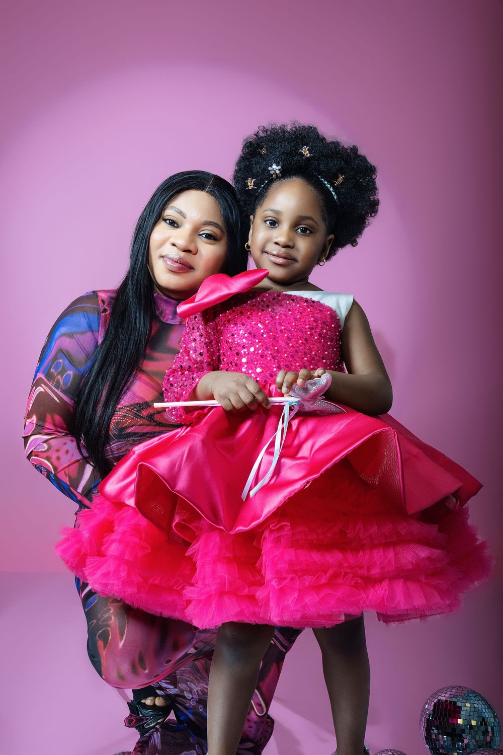 Sweet family moment with mother and daughter in coordinated outfits against pink backdrop.