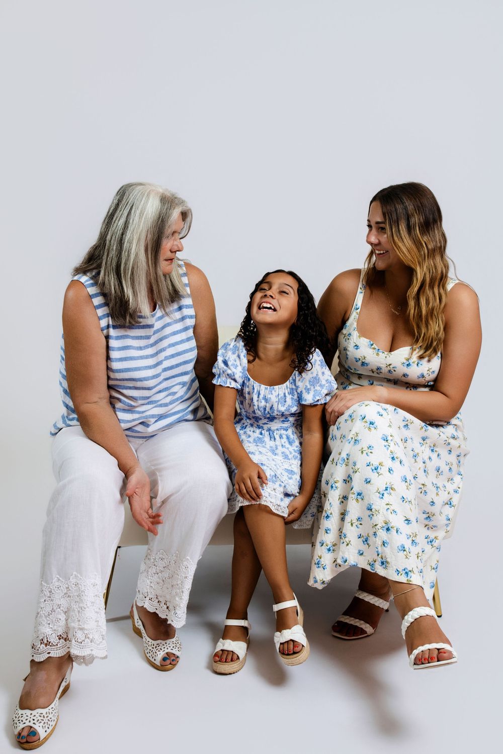 Three friends in coordinating blue and white summer outfits share joyful laughter while sitting together.