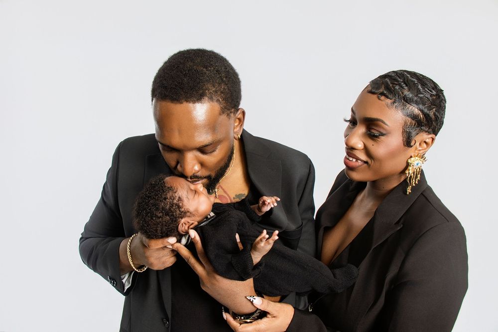 Family shares tender moment in formal black outfits against white background.