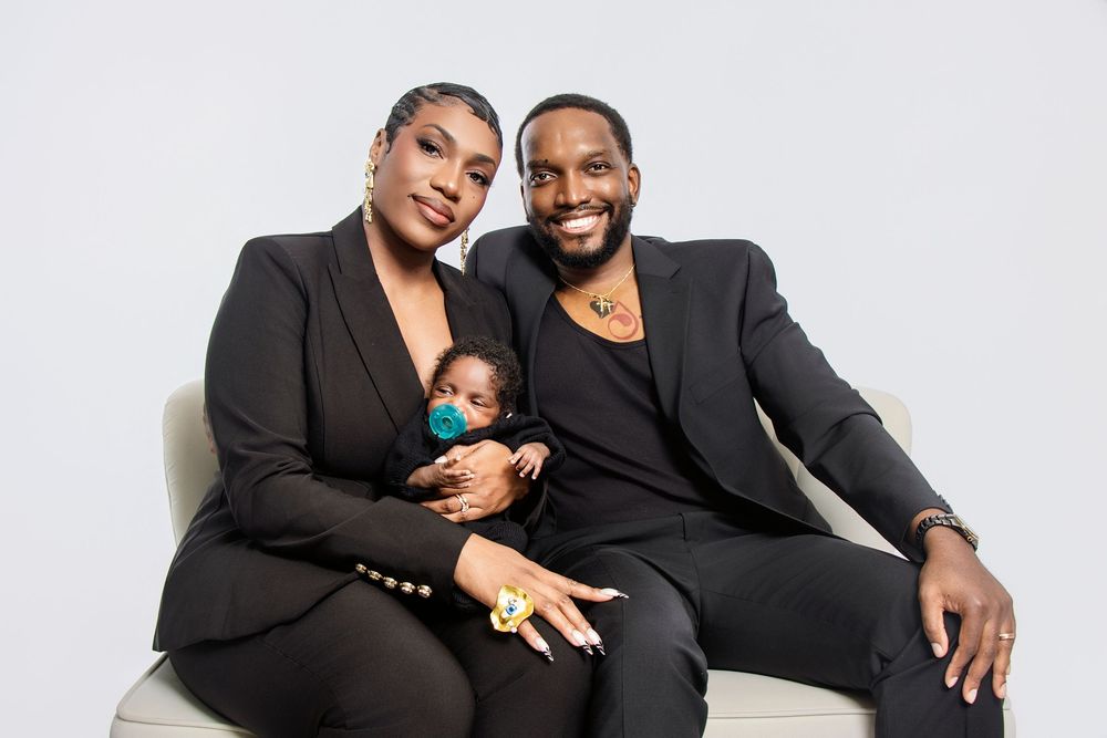 A couple in formal black attire poses together on a white background for a professional photoshoot.
