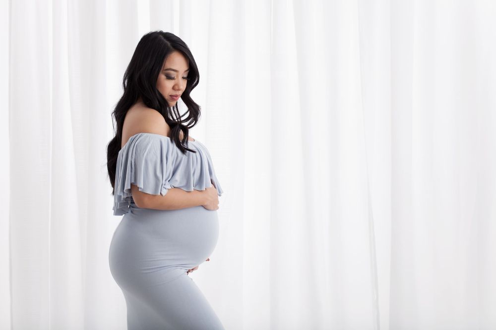 Side view maternity portrait showing pregnant woman in flowing gray dress.