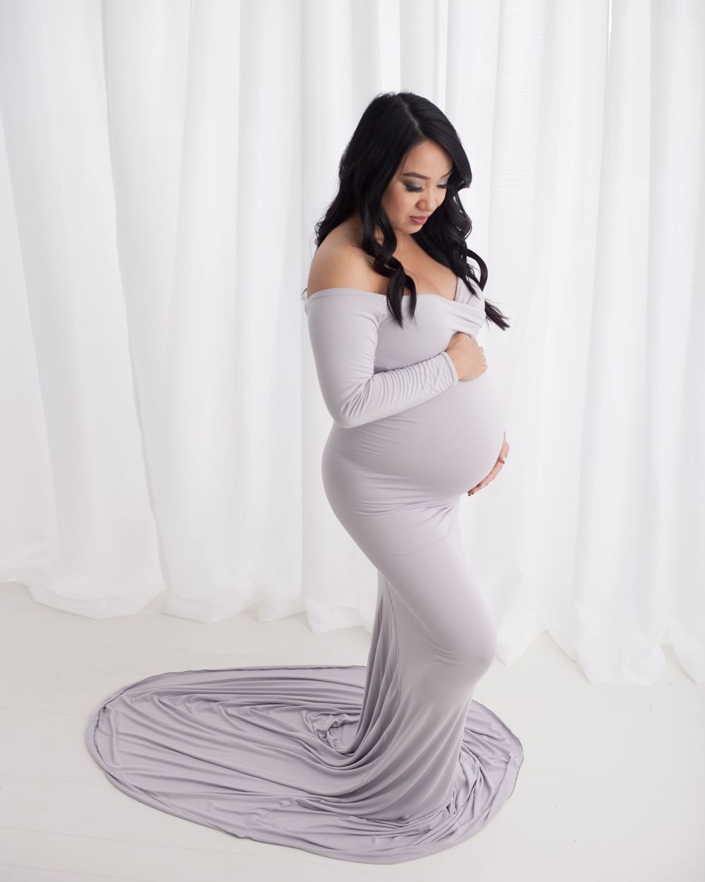 Elegant maternity photo of expecting mother in floor-length gray gown with dramatic train.