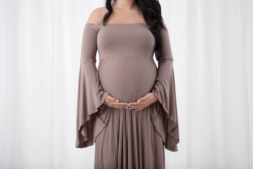 Maternity portrait showing pregnant woman in mauve bell-sleeve dress.