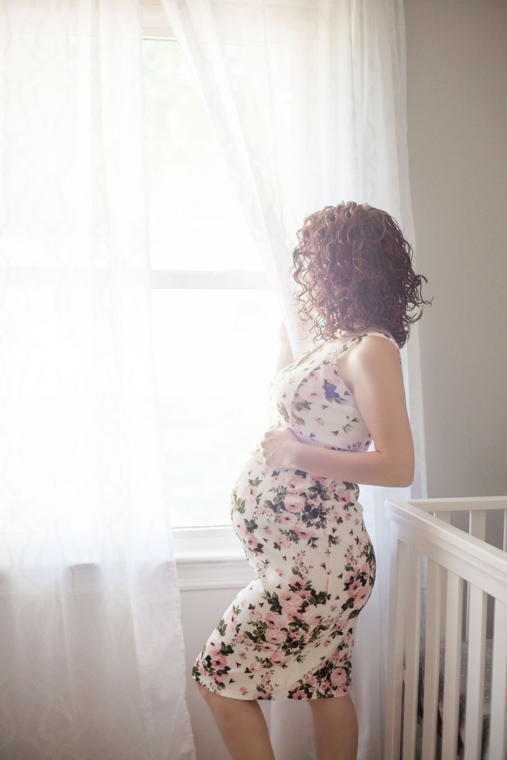 Silhouetted maternity portrait in floral dress by sunlit window.