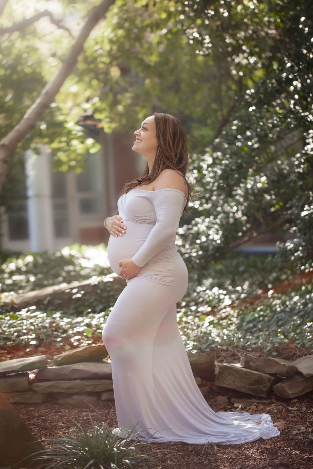 Ethereal maternity photograph in white dress amid blooming garden setting.