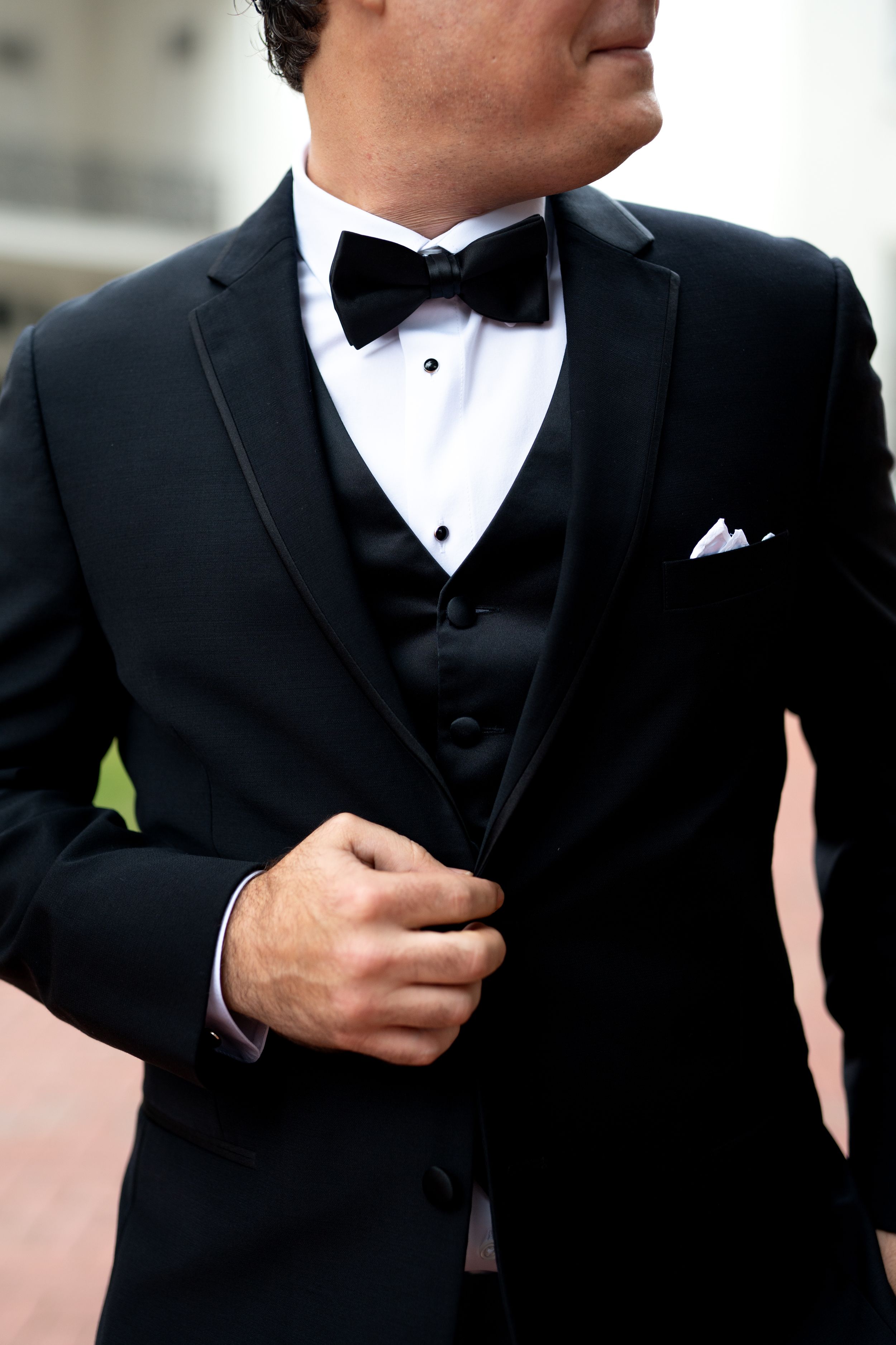 Close-up details of a groom's classic black tuxedo with bow tie and pocket square.