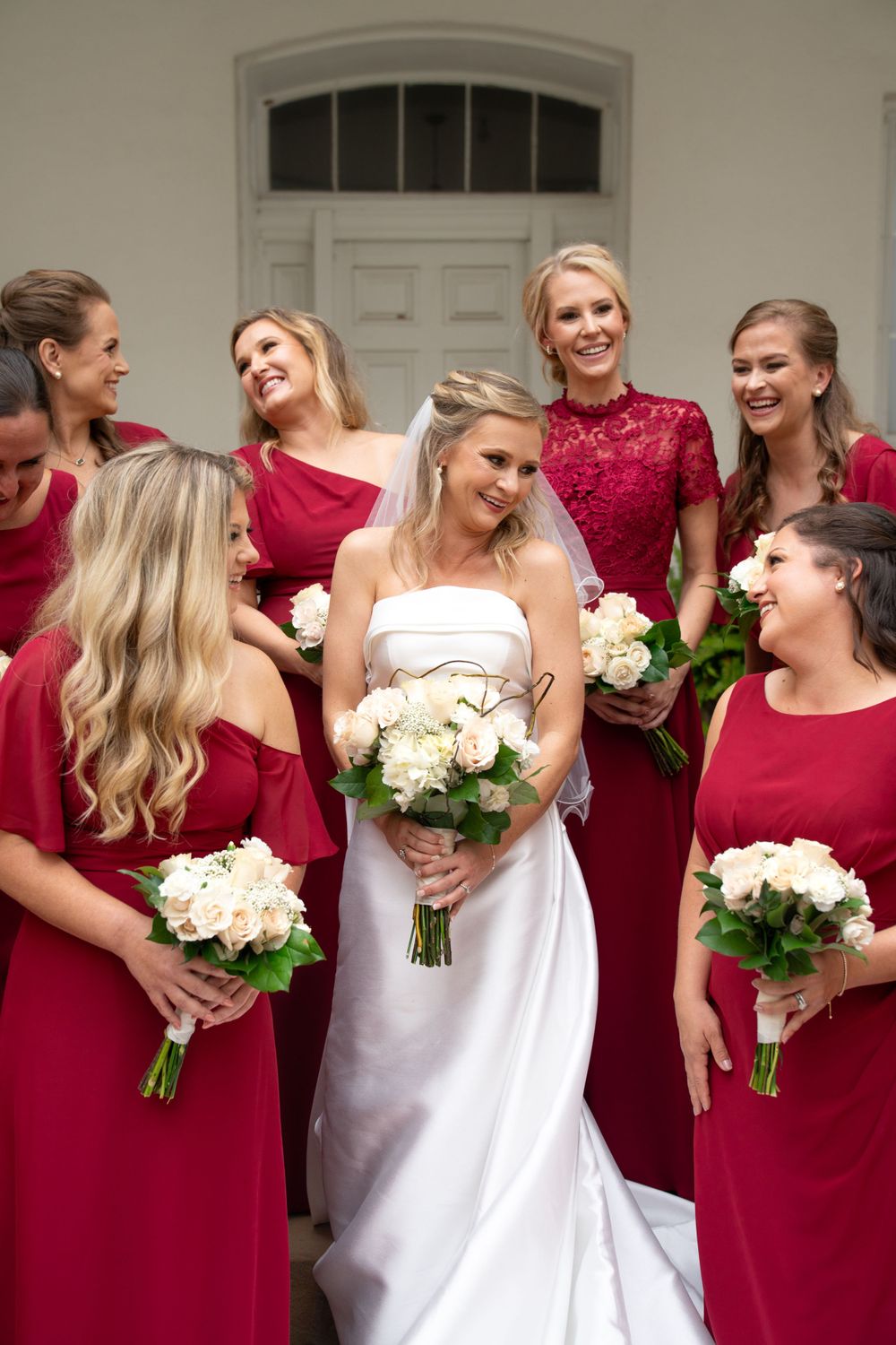 Bridesmaids in red dresses stand together holding white bouquets.