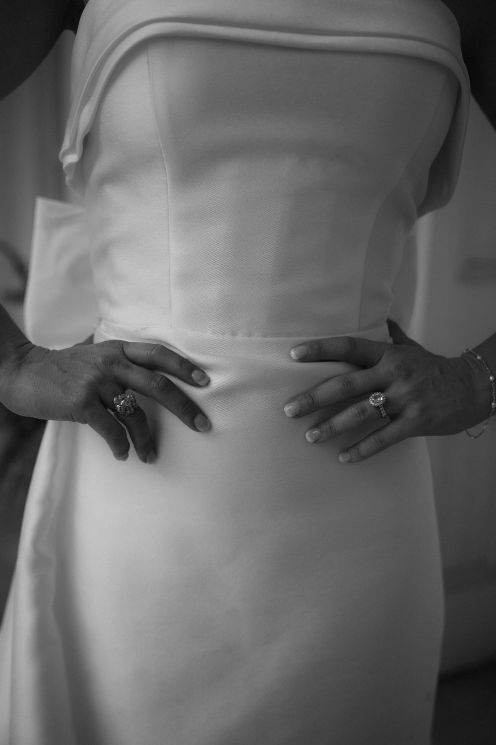 Close-up of hands touching white wedding dress fabric in black and white photography.