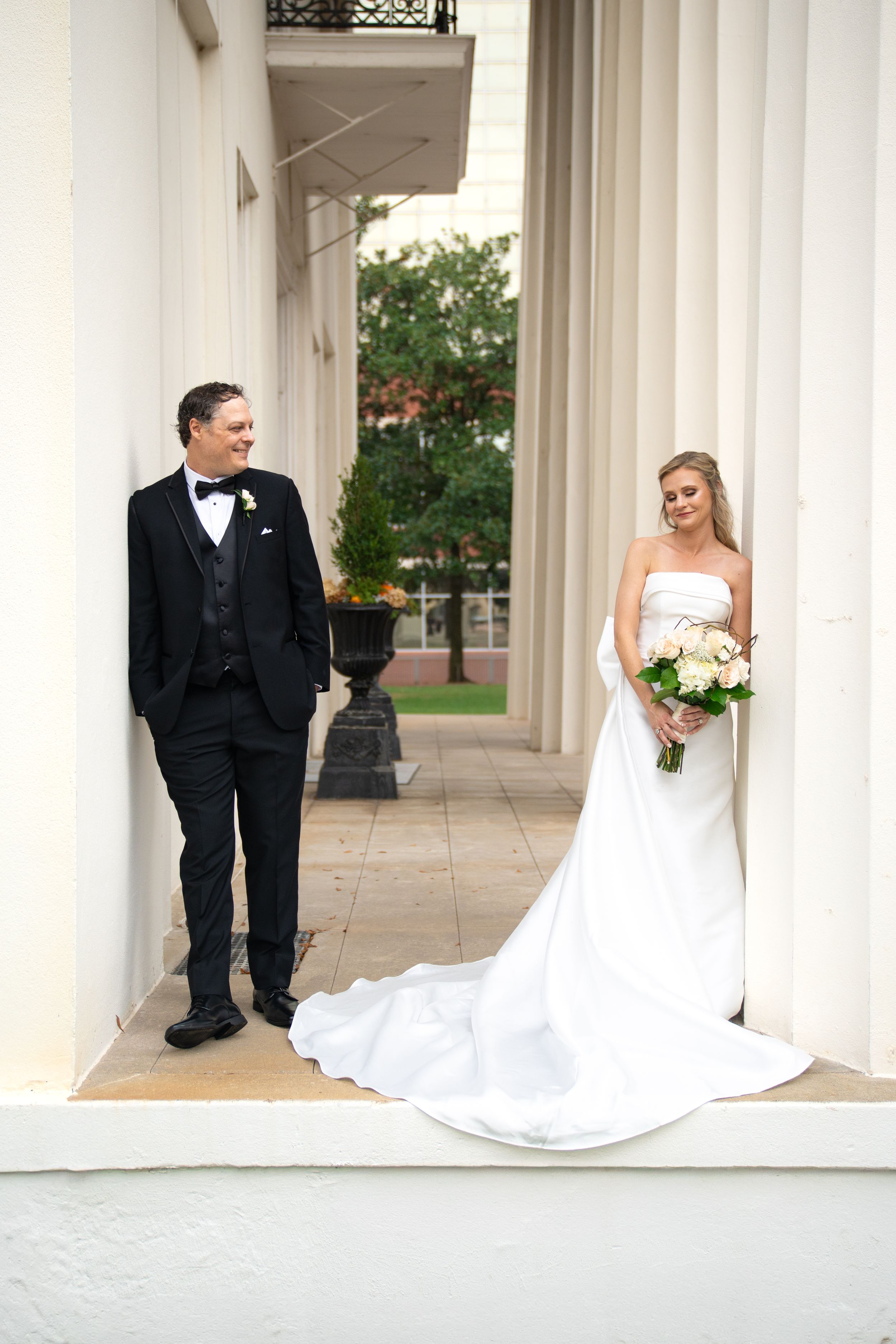 Wedding couple poses between white columns of classic building architecture.