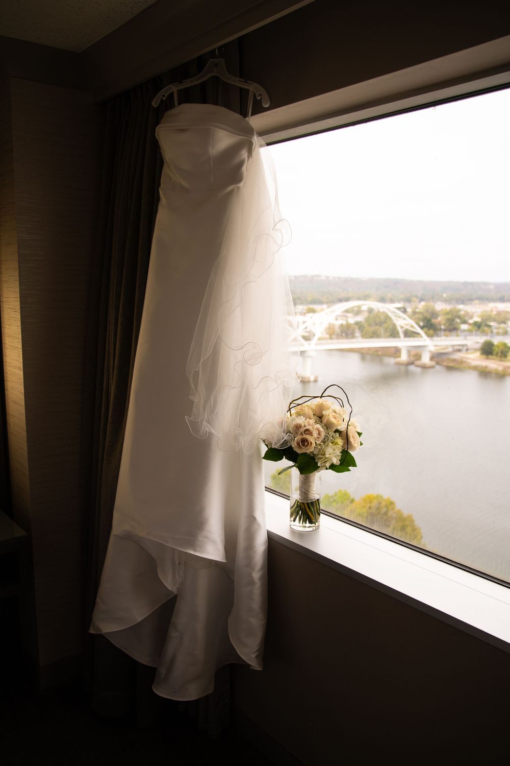 Wedding dress hanging by a window with natural light and scenic view in background.