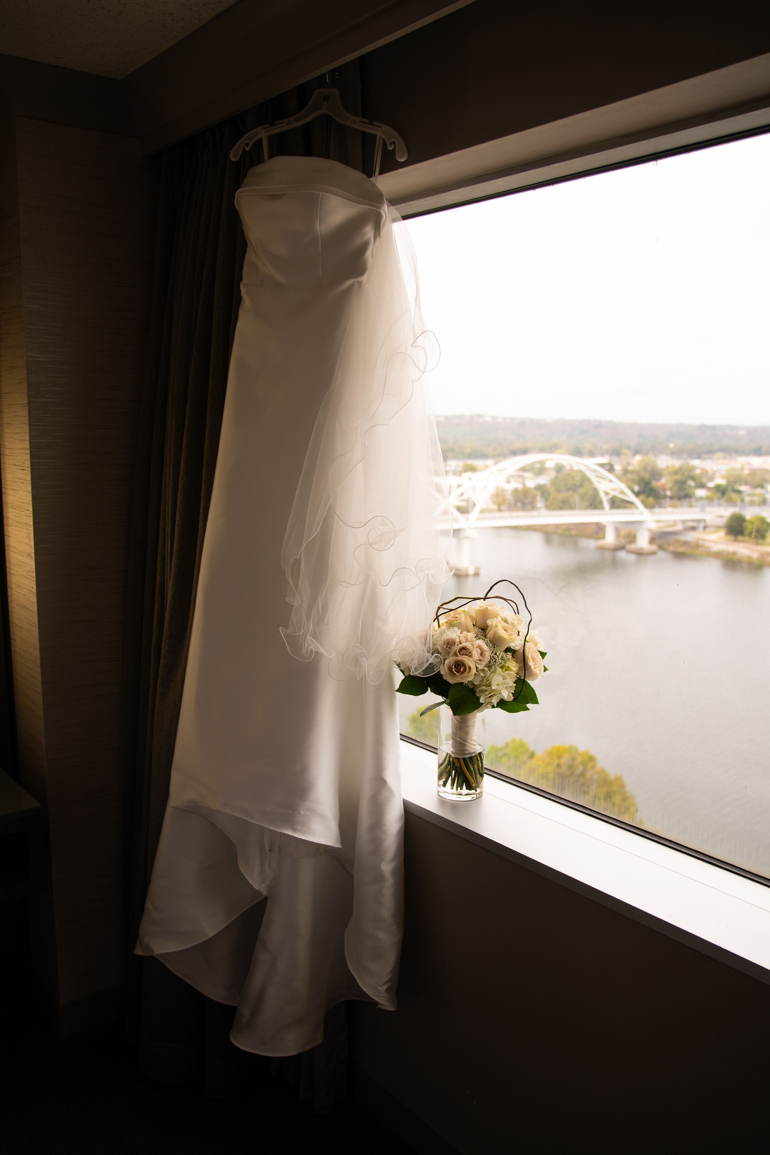 Wedding dress hanging by a window with natural light and scenic view in background.