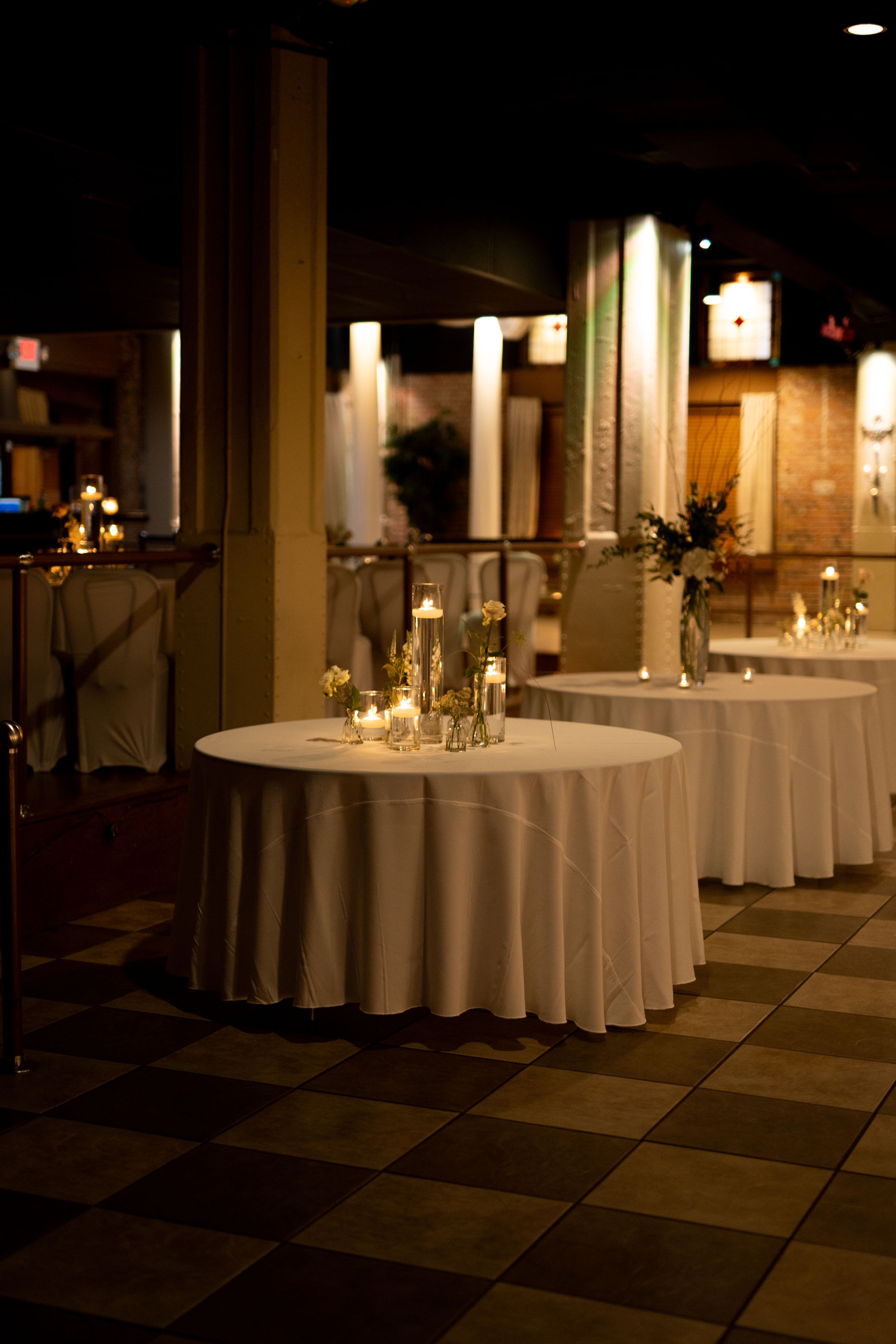 Elegant wedding reception setup with round tables, white linens and glowing candlelight centerpieces.