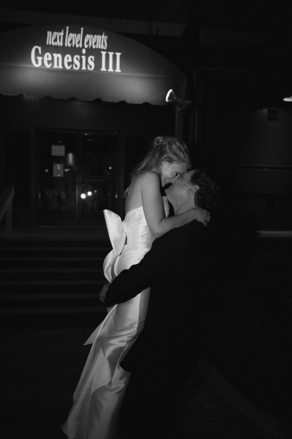 A romantic silhouette of newlyweds embracing in front of illuminated signage.