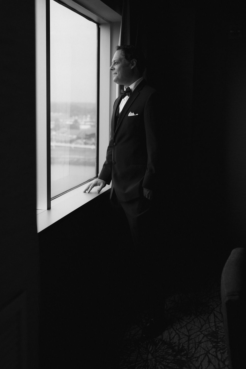 Silhouette of a figure in formal attire standing by a window in a dark room.