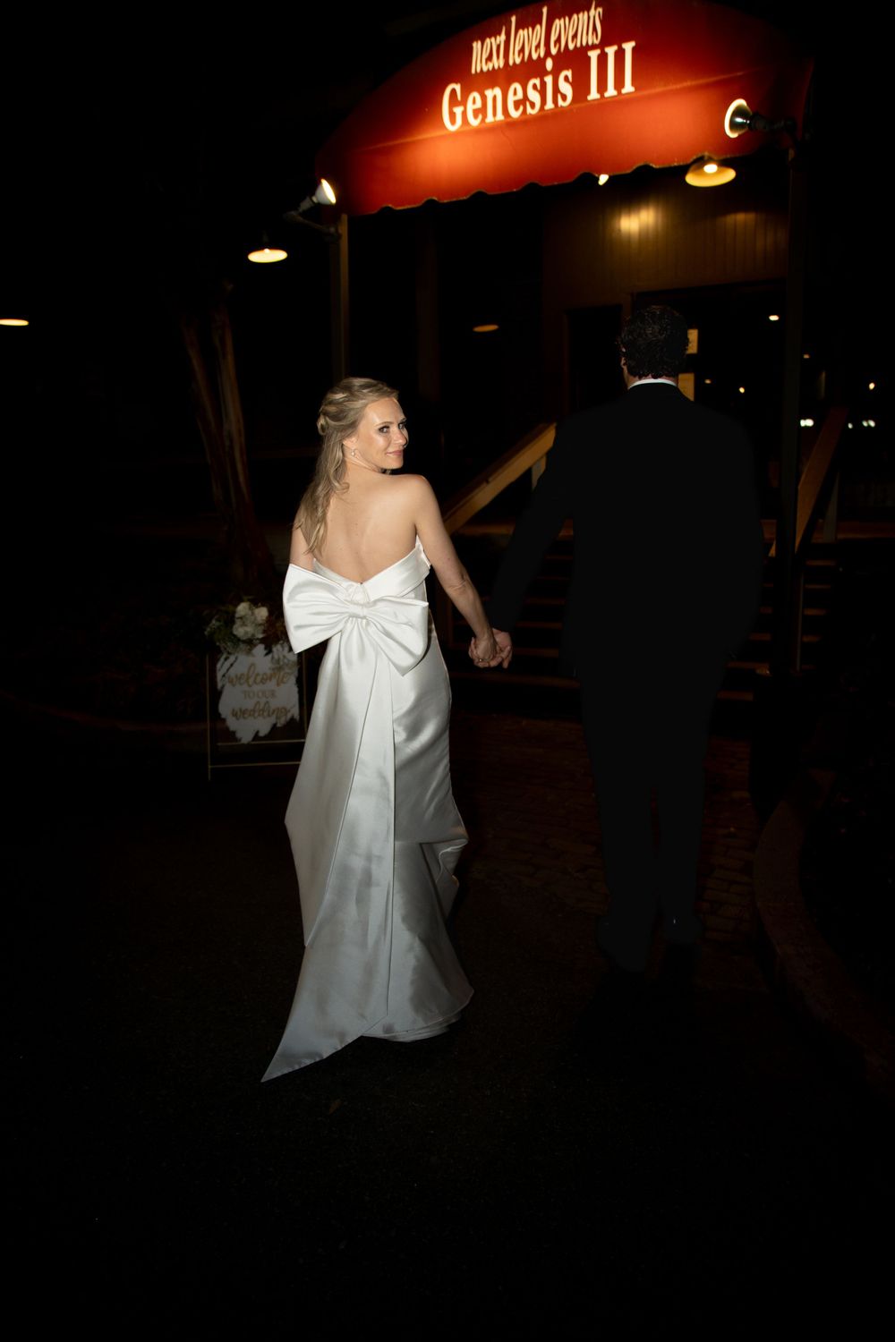 A couple dances underneath illuminated signage at a nighttime wedding venue.