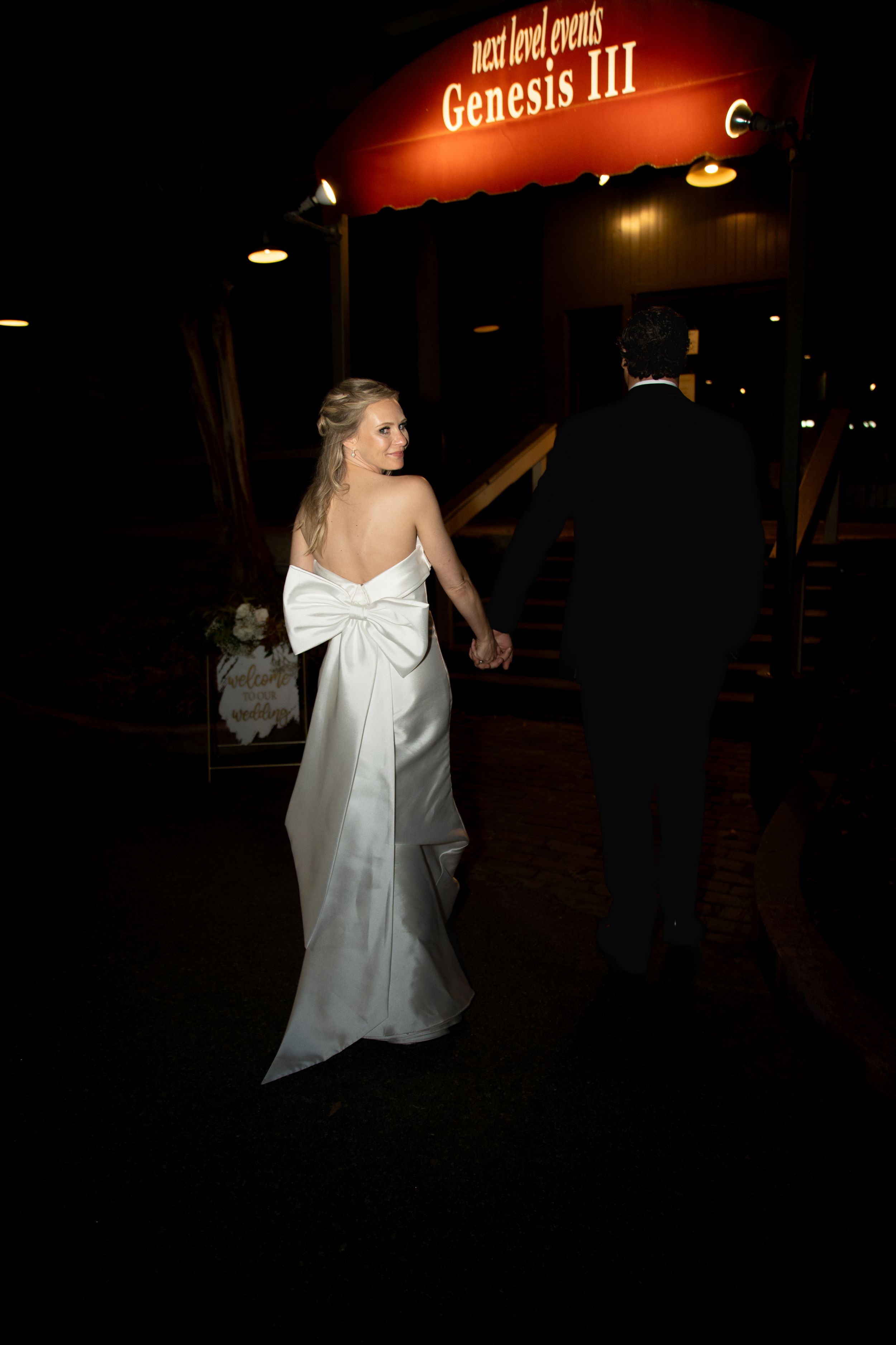 A couple dances underneath illuminated signage at a nighttime wedding venue.