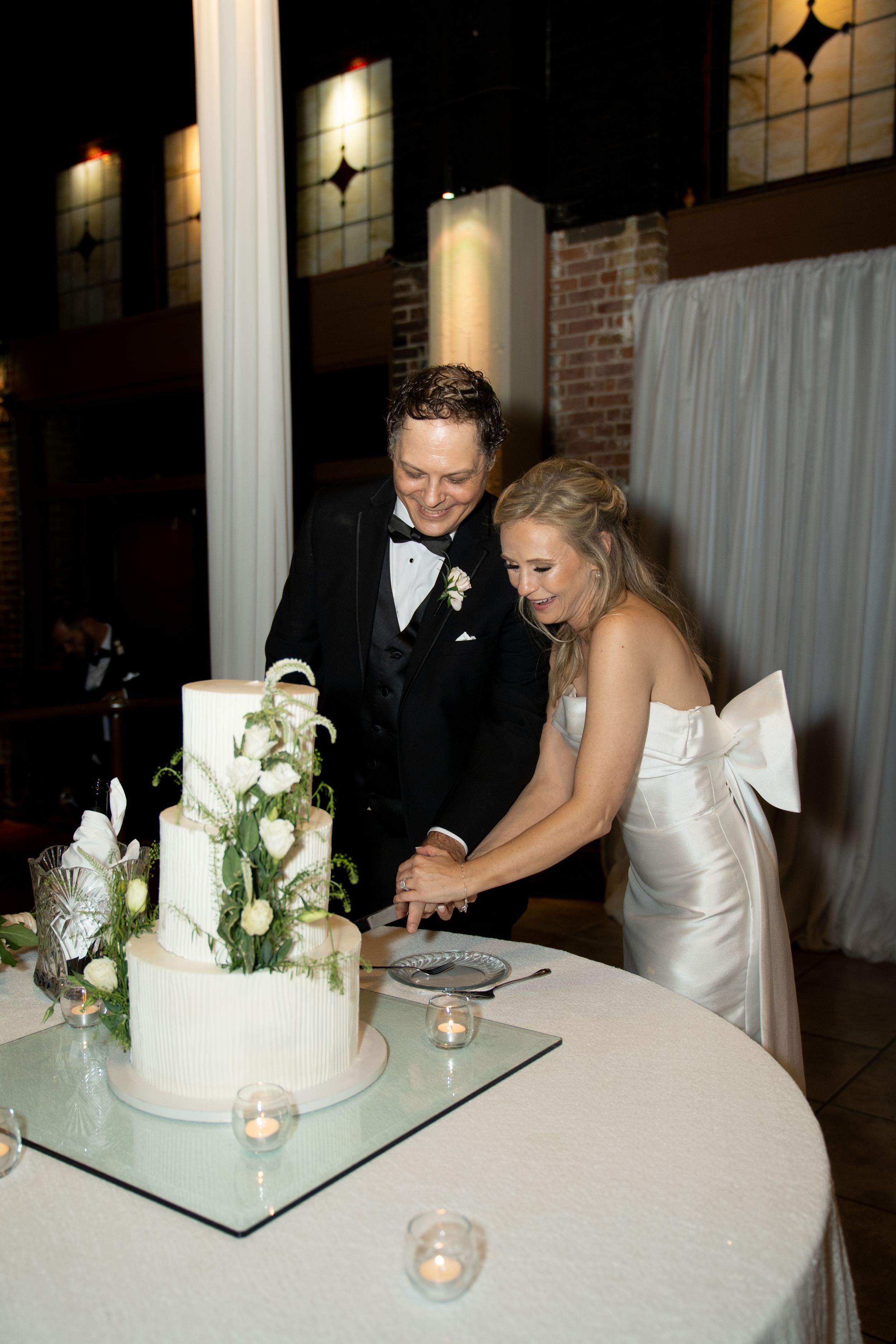 Wedding cake cutting ceremony at reception with white floral decorations.