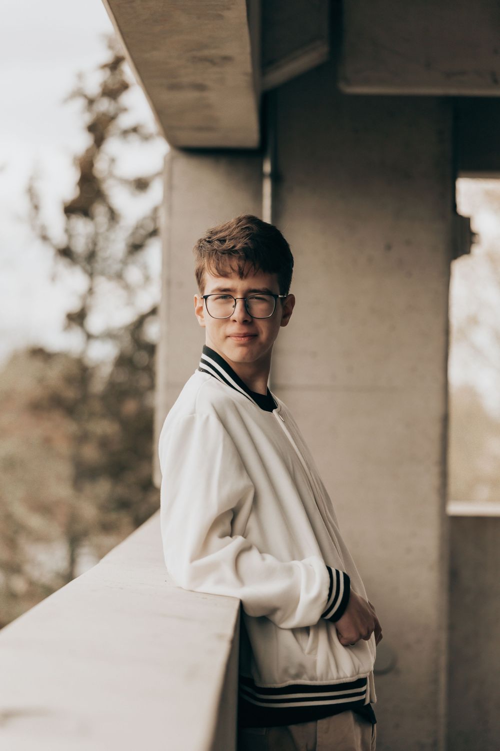 A retro varsity jacket in white with dark trim worn on a balcony during golden hour creates a nostalgic aesthetic.