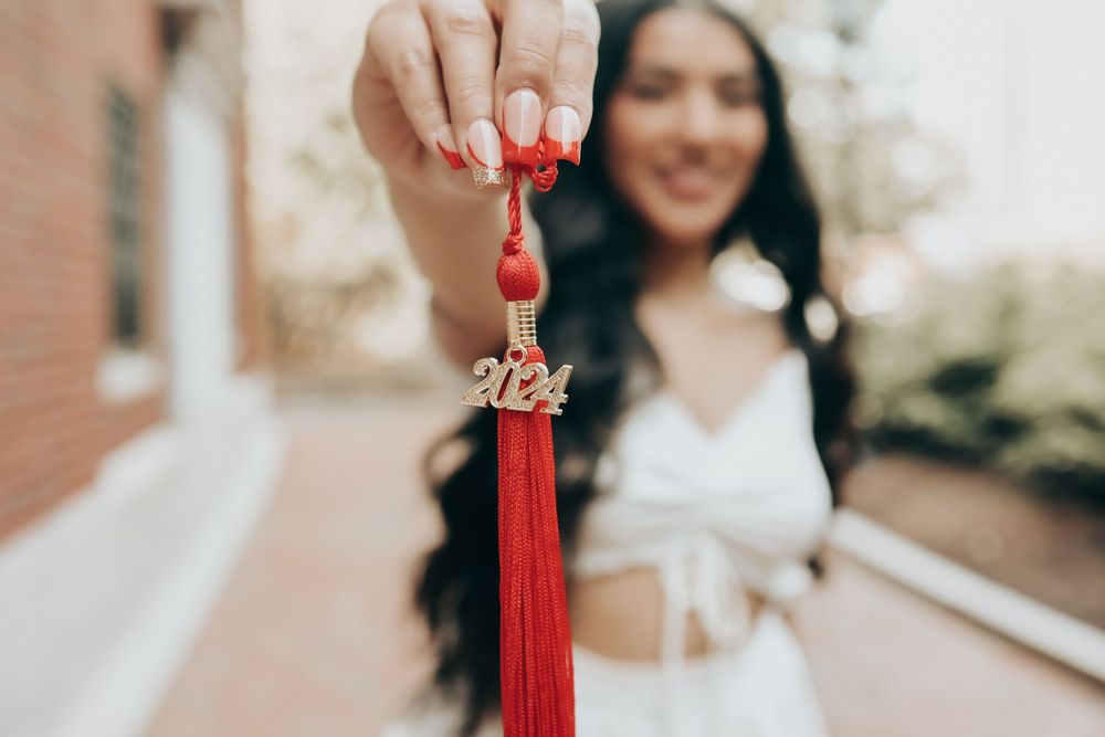 Red graduation tassel held up against blurred outdoor background.