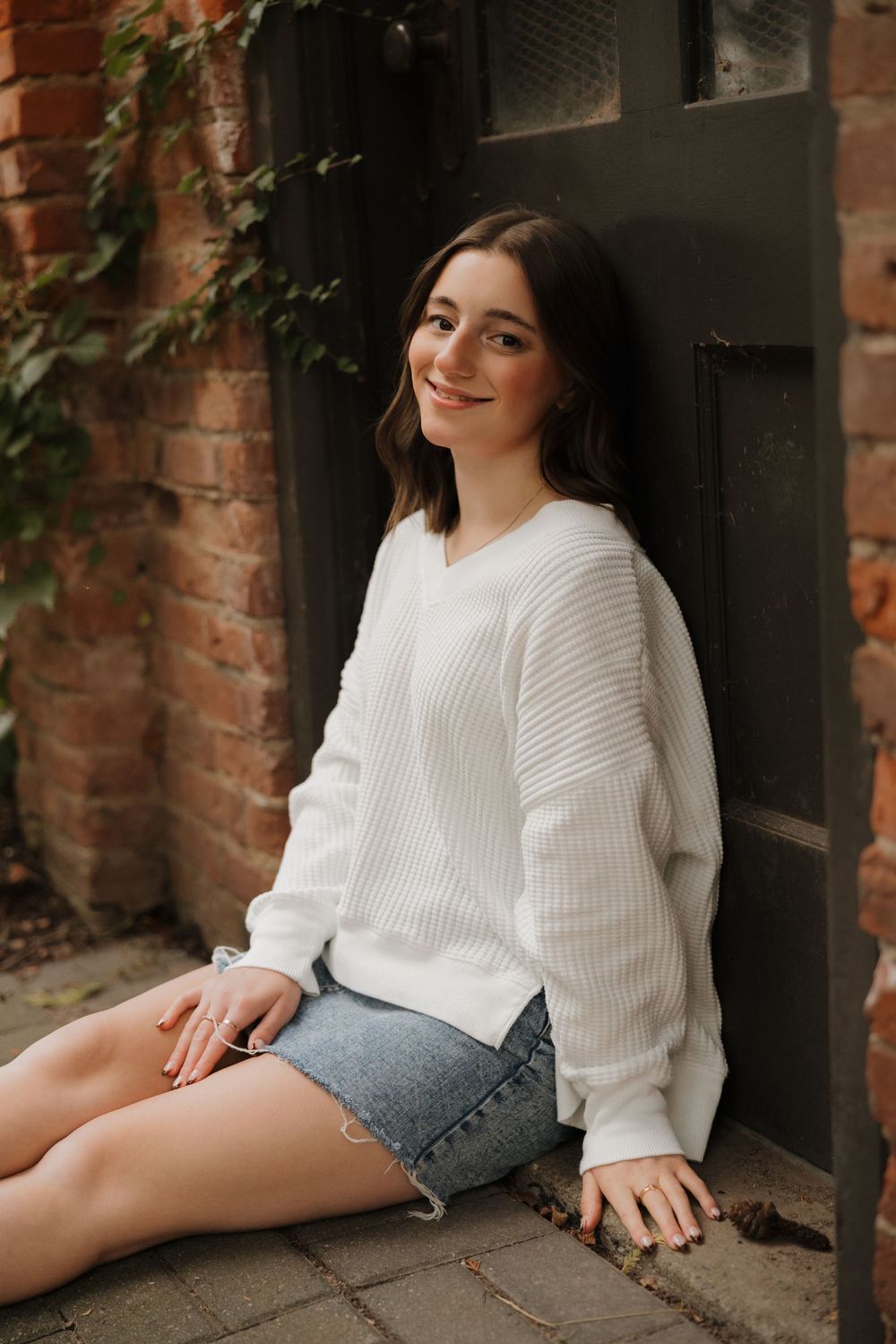 Casual outdoor portrait session against brick wall featuring white sweater and denim shorts.