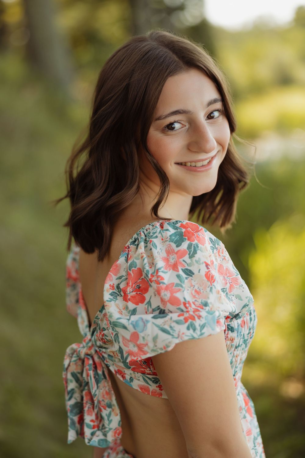 A woman in a floral print dress with cutout back poses outdoors in soft natural lighting.