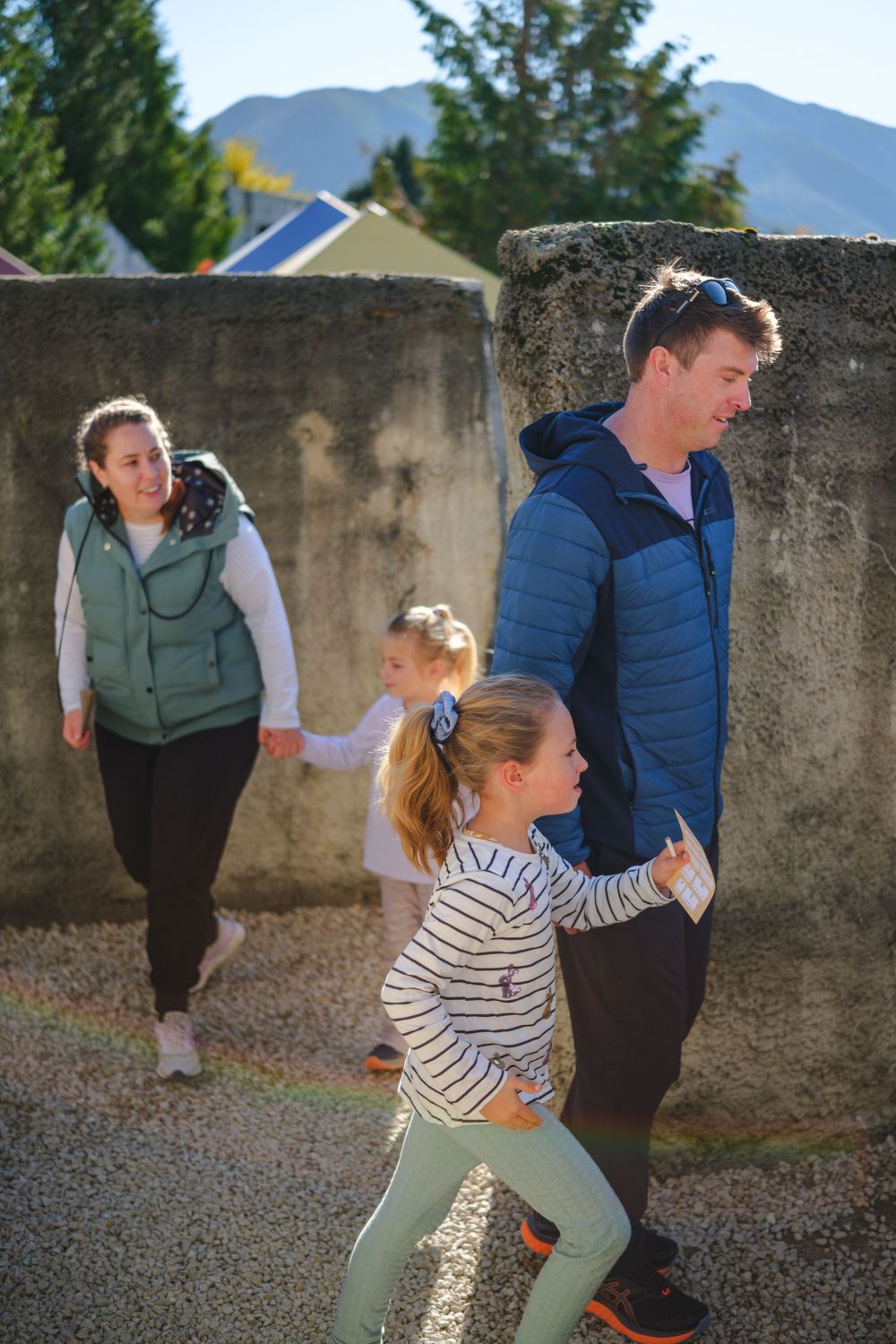 Mini golf players lined up along a concrete wall with mountains visible in the background.