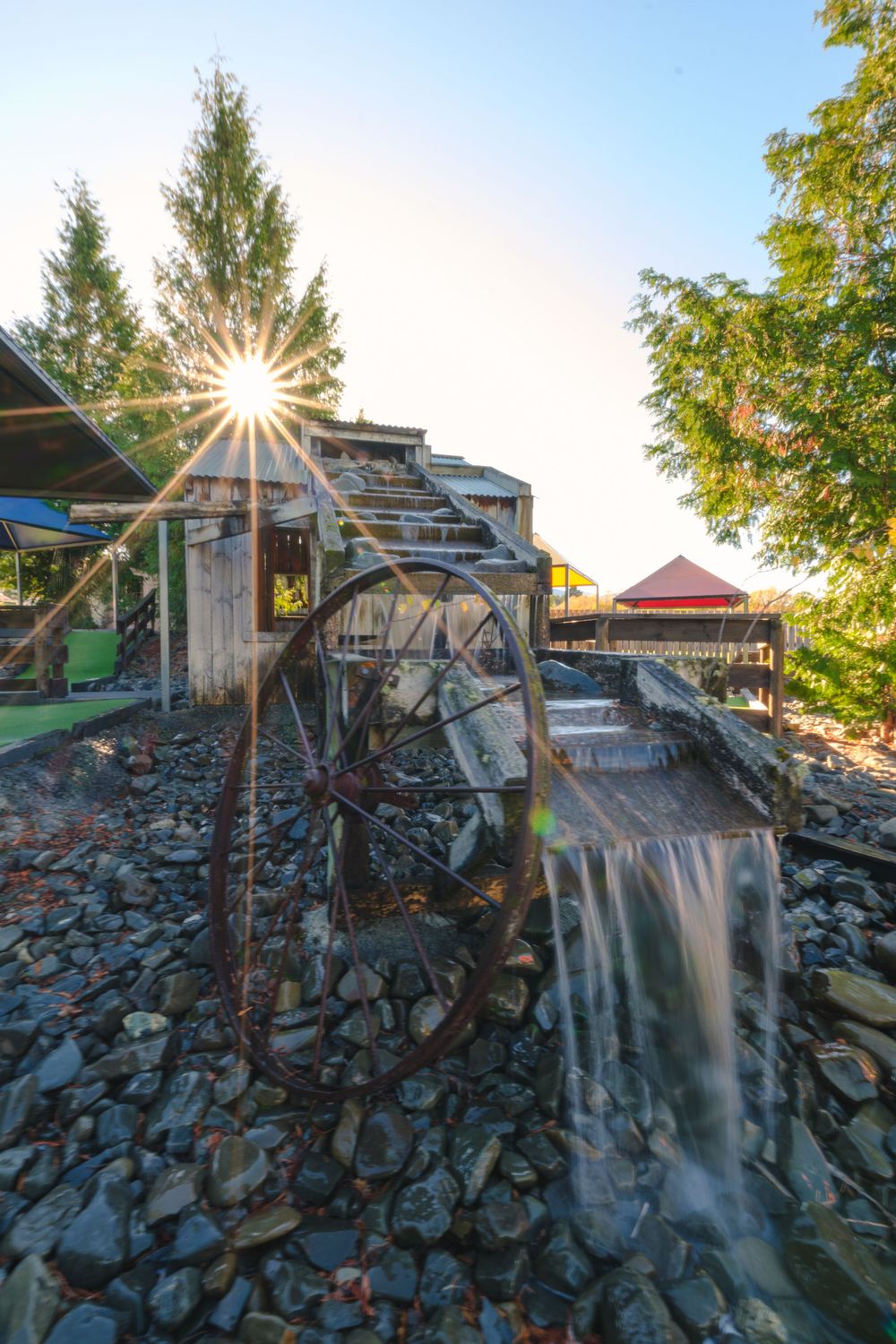 Miniature golf water feature with cascading waterfall over stone wall during golden hour.