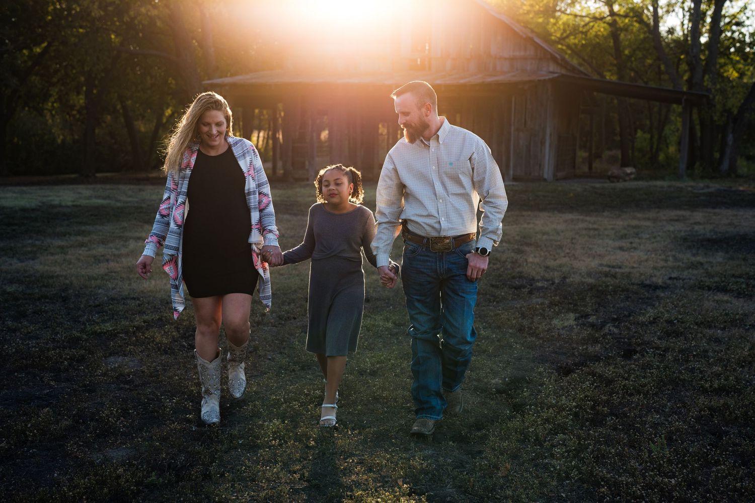 Family walks hand in hand during sunset with rustic barn in background.