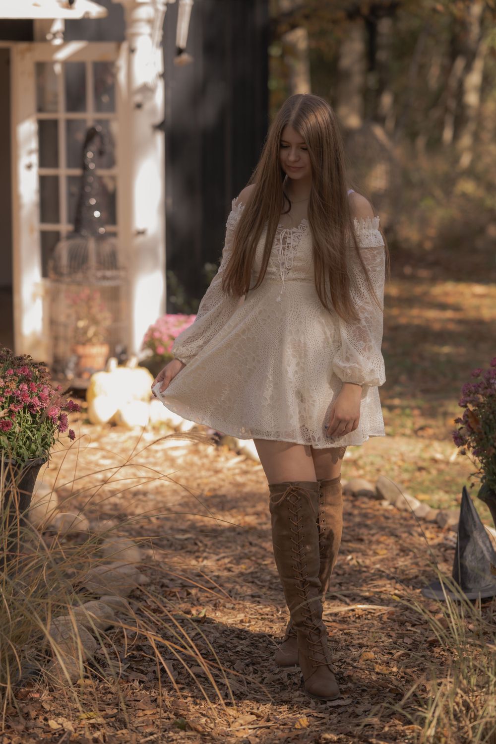 A white lace dress and brown knee-high boots create a romantic autumn look in a garden setting.