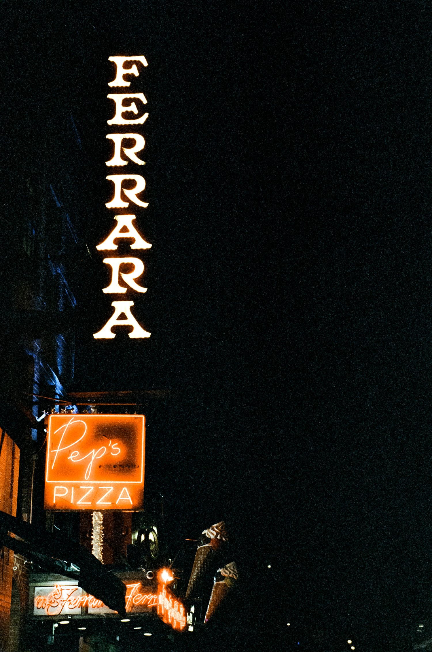 Vintage neon signs for Ferrara and Pepe's Pizza glowing against dark night sky.