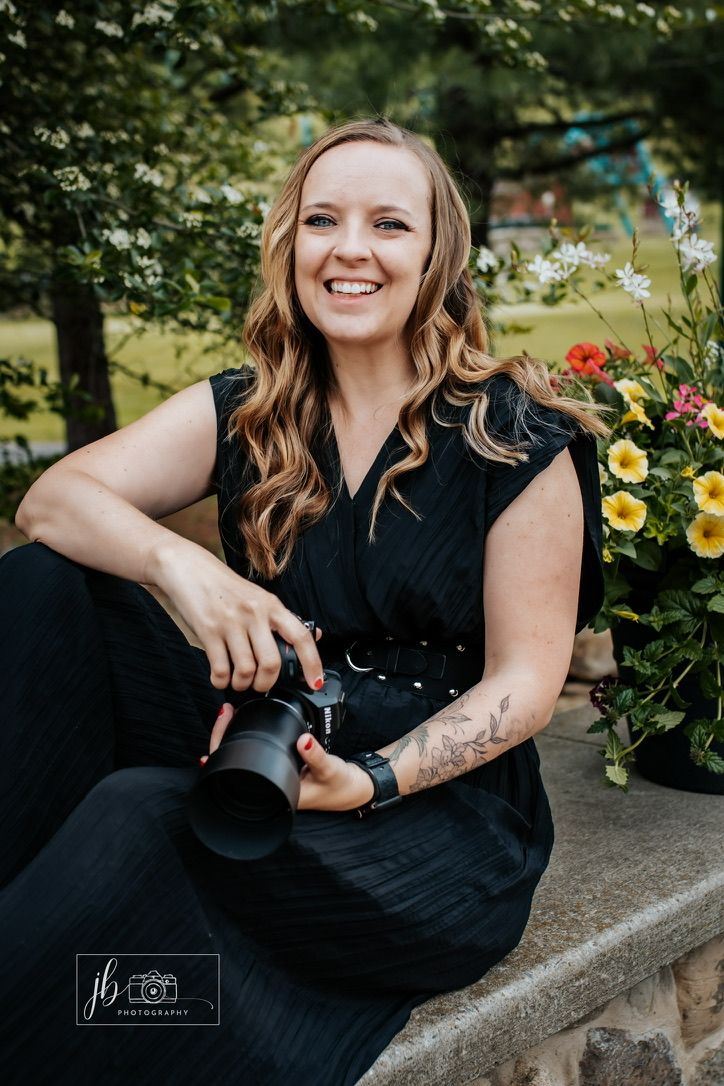 Photographer holding camera lens in bright studio with decorative greenery and natural lighting.