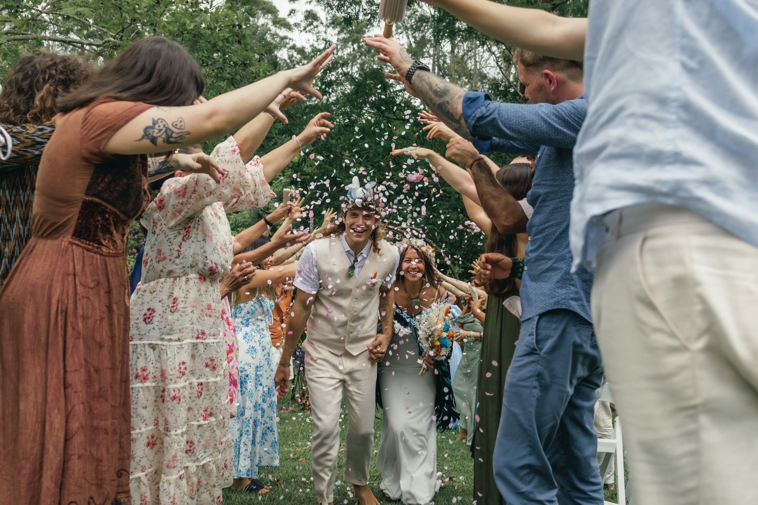 Wedding guests celebrate by forming a tunnel with raised arms for the newlyweds to pass through outdoors.