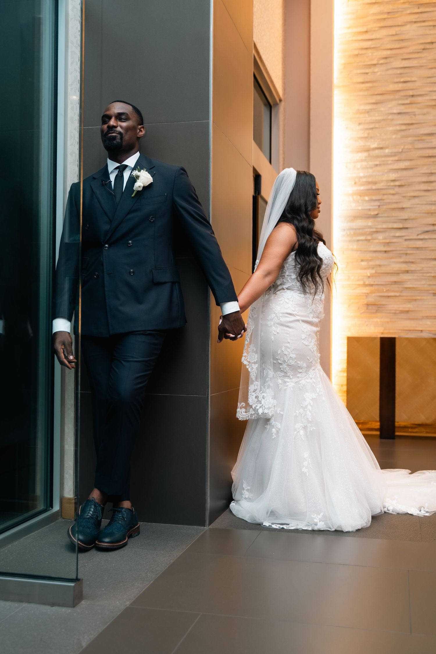 Creative wedding photo of couple standing against modern interior wall.