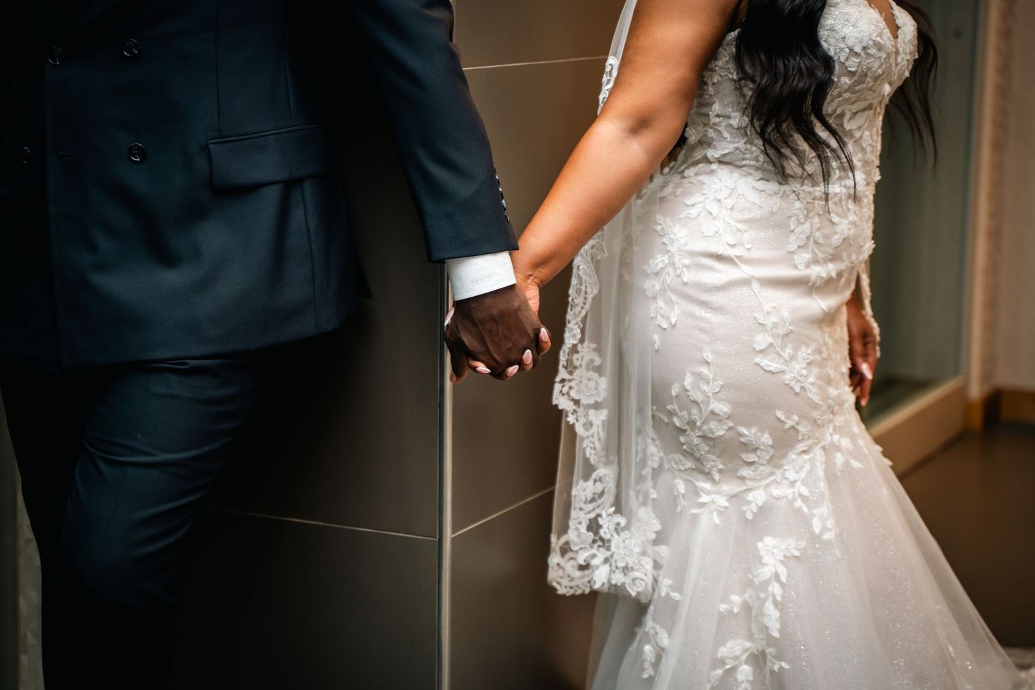 Close-up of newlyweds holding hands showing details of dress and suit.