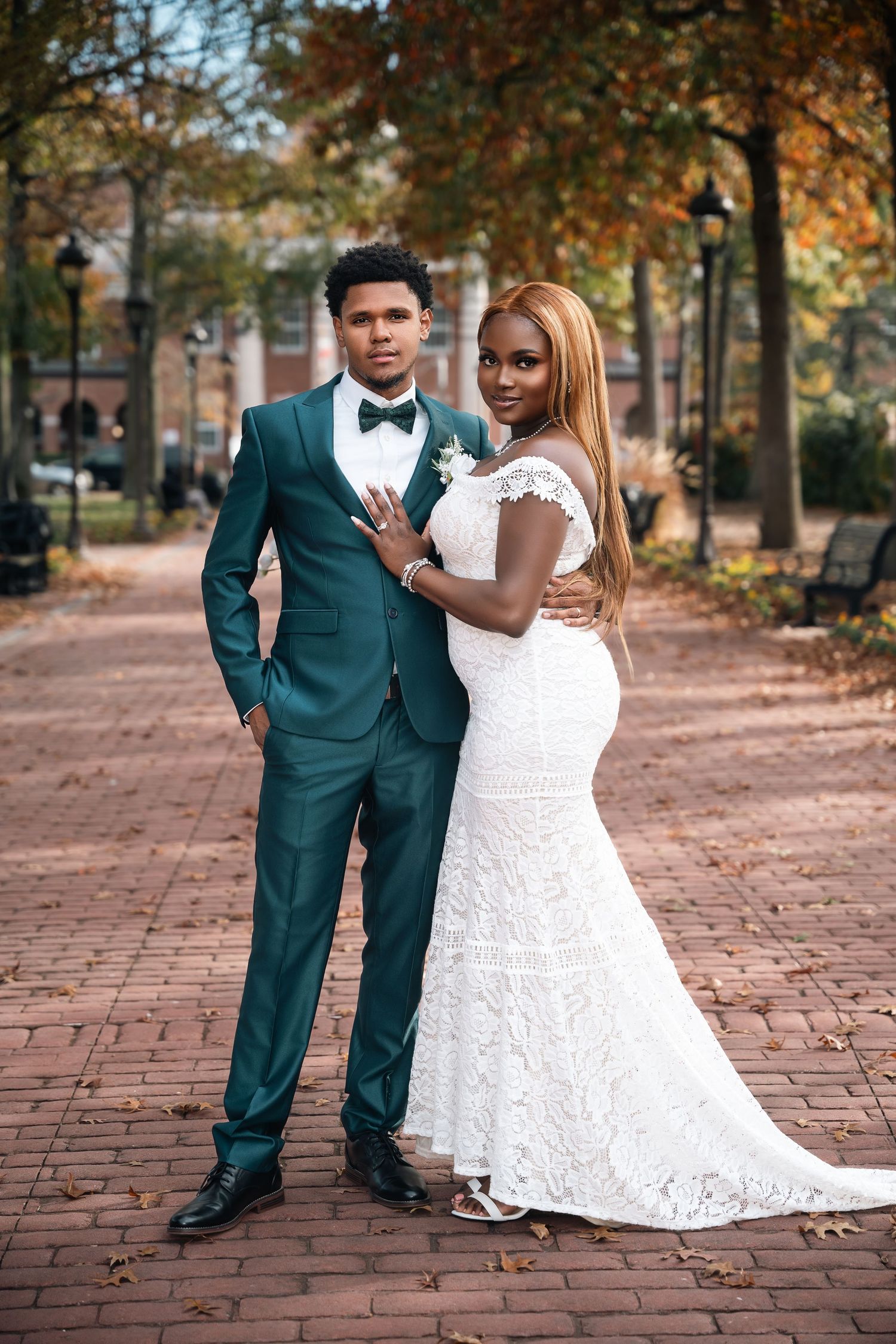 Stunning newlyweds pose on brick pathway surrounded by autumn trees.