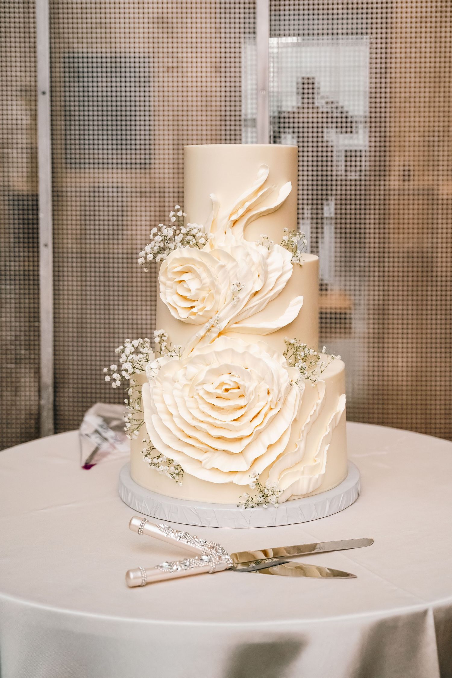 Elegant white wedding cake decorated with large sugar roses and baby's breath on round table.
