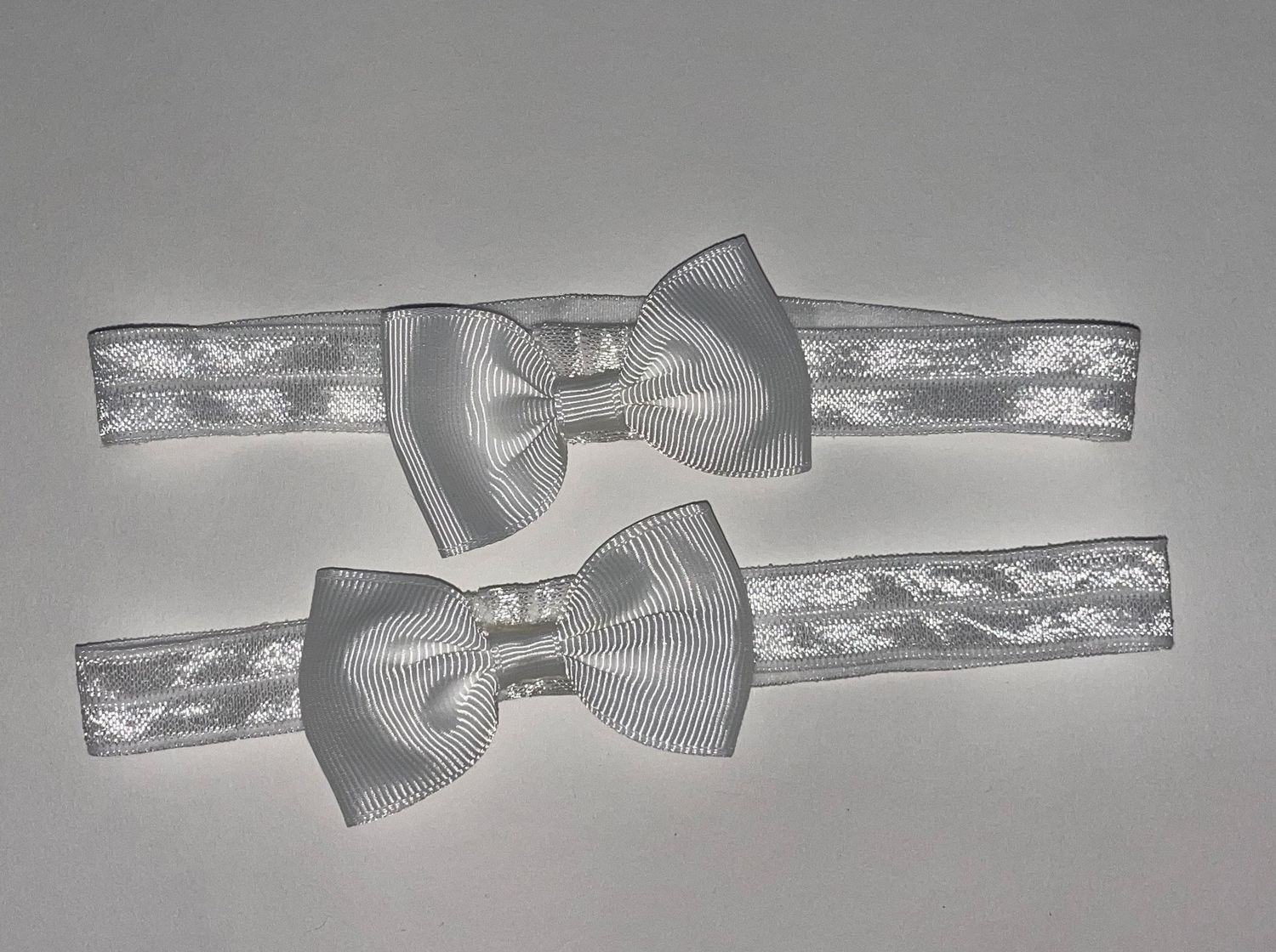 Row of white satin bow ties attached to elastic headbands.