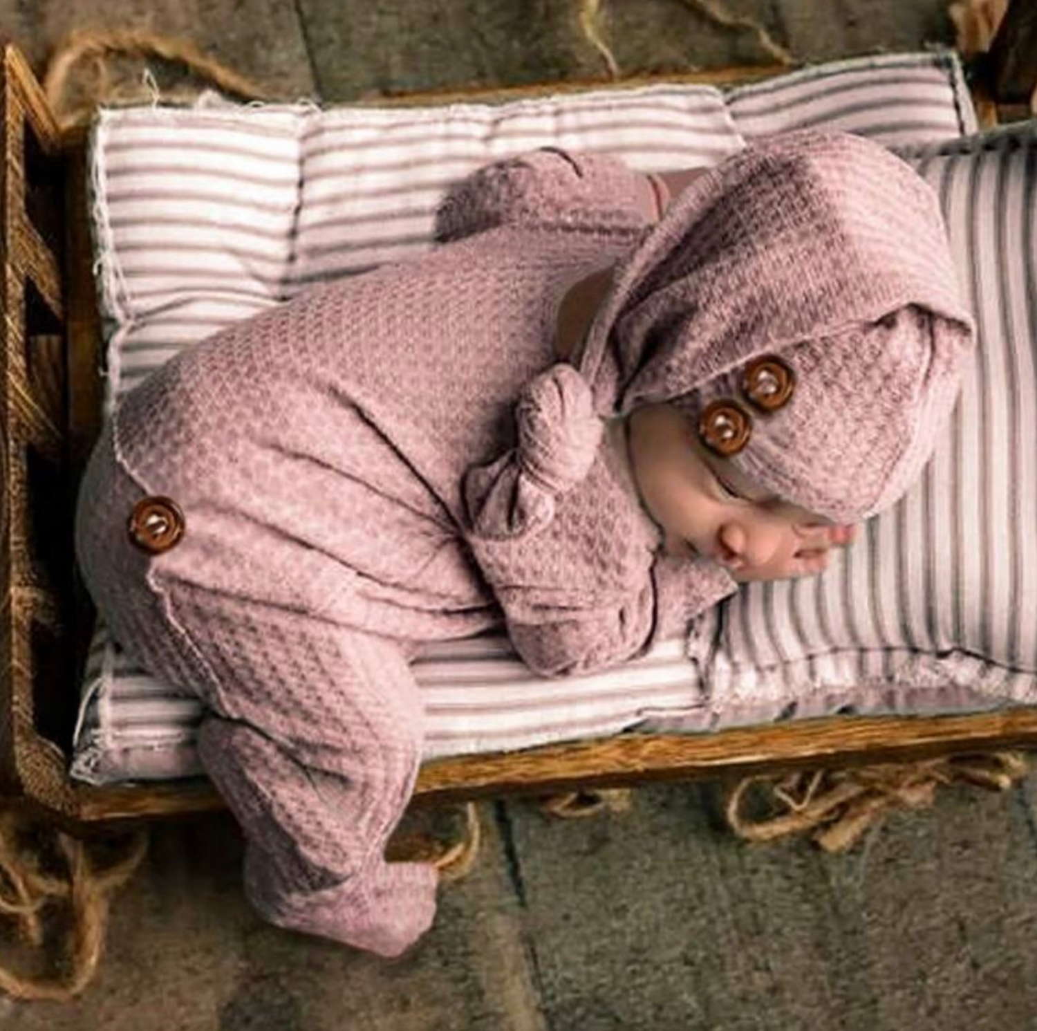 Cozy striped bedding and pink knit outfit arranged for newborn photography.