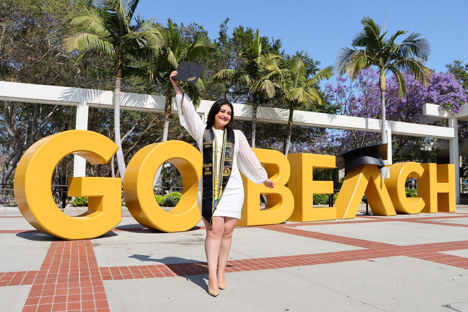 Graduate poses in front of large yellow GO BEACH letters outdoors.