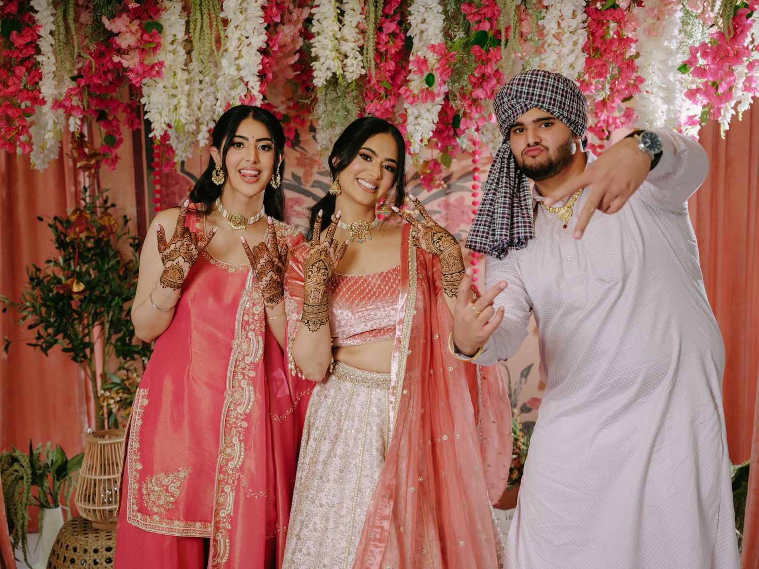 Group photo against floral backdrop with decorative pink and white flowers and traditional cultural attire.